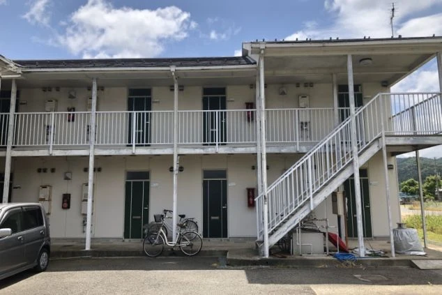 リゾートバイトで提供されるアパート寮の外観の画像。2階建ての建物で、外階段と廊下があり、自転車も駐輪されている。