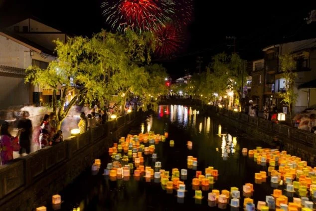 夜の城崎温泉の川に灯籠が浮かび、上空には花火が打ち上がる美しい風景。夏祭りやイベントが盛んな温泉地でのリゾートバイトで、日本の伝統的な行事を楽しめる画像。