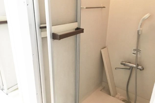 シンプルなシャワールームの画像です。シャワーヘッドと棚があり、寮の共同シャワー施設のイメージが伝わります。