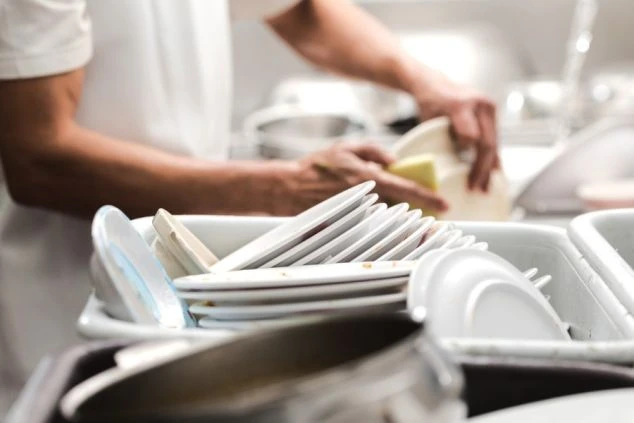 厨房のシンクで白い皿を洗う手元が映るイメージ画像。リゾートバイトの洗い場業務の様子。