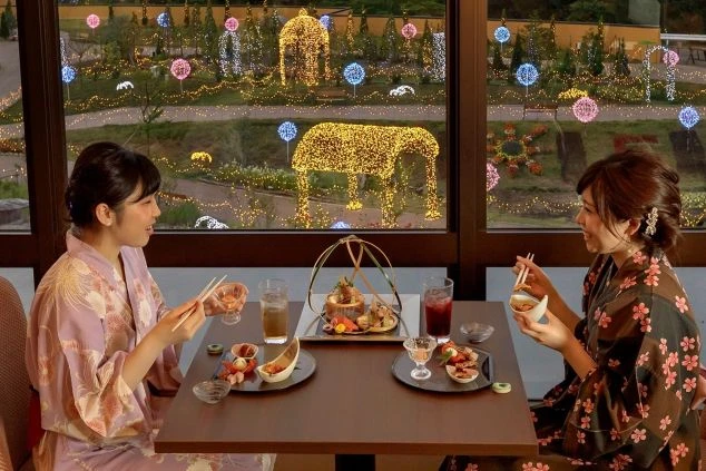 鶯宿温泉にあるホテルのレストランで、色とりどりのイルミネーションを背景に食事を楽しむ女性たちの画像。浴衣姿で会話を交わしている。