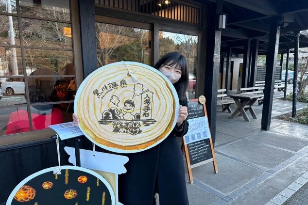 黒川温泉の「入湯手形」の看板を持って笑顔を見せる女性の画像。温泉地のリゾートバイトで休日を満喫するイメージ。