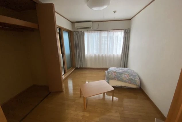 リゾートバイトの個室寮の室内。フローリングの床に布団とローテーブル、クローゼットが備え付けられており、窓からは光が差し込む明るい部屋の画像。