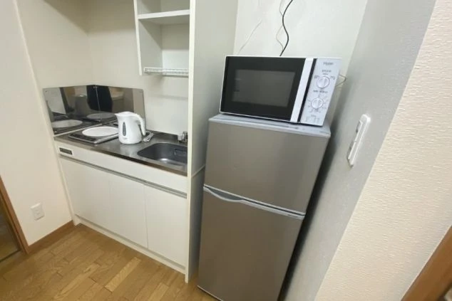 リゾートバイトの個室寮に備え付けられたミニキッチン。IHクッキングヒーターとシンク、電子レンジ、冷蔵庫があり、自炊に便利な設備の画像。