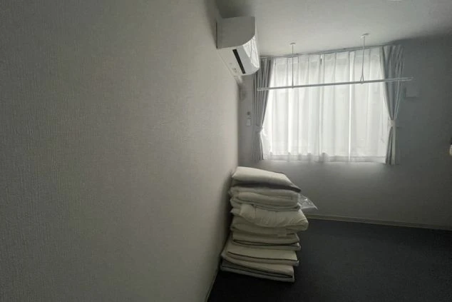 リゾートバイトの個室寮の室内。積み重ねられた布団とエアコン、窓があり、プライベートな空間で休める設備の画像。