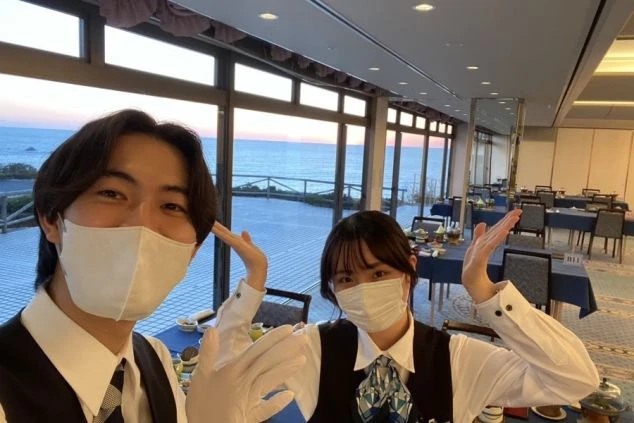 海が見えるレストランで働く男女スタッフ2名のセルフィー。職場の雰囲気の良さをアピールする画像。
