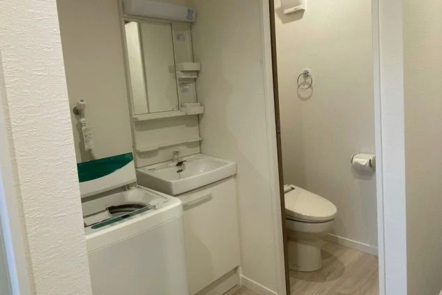 寮のサニタリールーム。洗面台と洗濯機、独立したトイレが設置され、使い勝手の良い水回り。