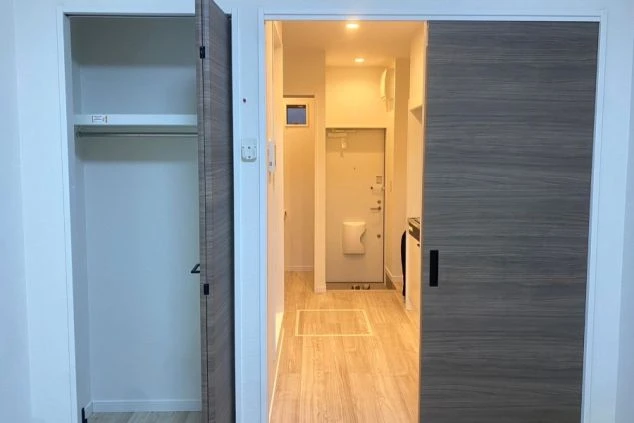 寮の居室から玄関方向を見たところ。左手には収納スペース、奥には玄関ドアとトイレが見える。