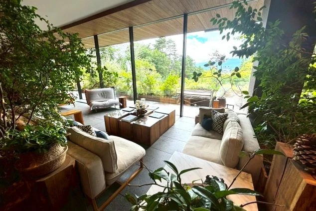 夕暮れの富士山をスマートフォンで撮影する人物の後ろ姿。手前には駐車場とフェンスが見える。