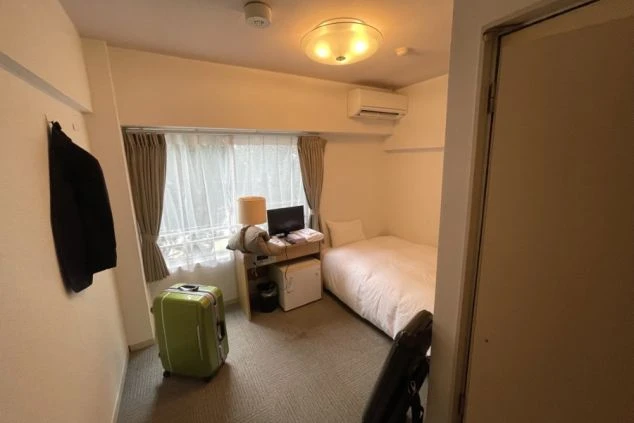 リゾートバイトの個室寮の室内。シングルベッド、テレビ、ミニ冷蔵庫、スーツケースが置かれ、すぐに生活を始められる設備の画像。