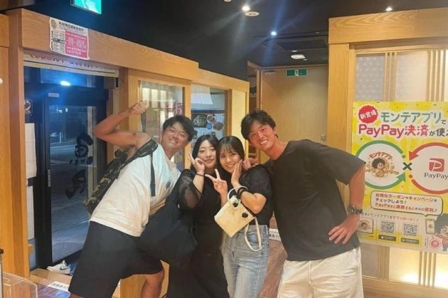 飲食店内で、笑顔でポーズをとる4人の男女。リゾートバイトで新しい出会いや仲間との楽しい時間を過ごしたい方、PayPay決済対応の店舗で働きたい方に訴求するワクトリスタッフが撮影したオリジナル画像。