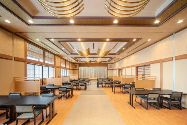 和室の宴会場のようなレストランの画像。多くのテーブルと椅子が並び、奥にはステージが見える。リゾートバイトの職場となる施設の雰囲気。