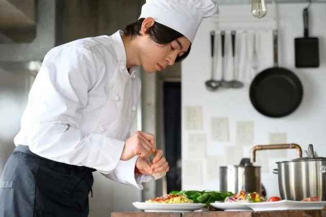 料理に調味料をかけるシェフ。厨房で食事の盛り付けをしている様子。
