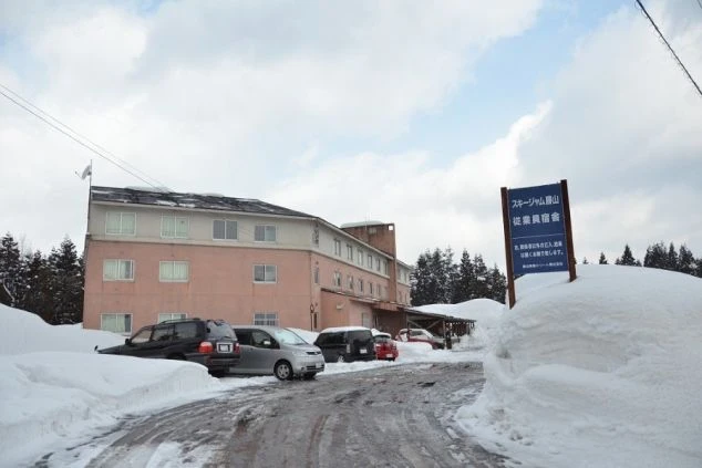 雪に覆われた道を挟んで建つ、スキー場の従業員宿舎。冬のリゾートバイトで、ゲレンデに近く住み込みで働ける寮の外観の画像。