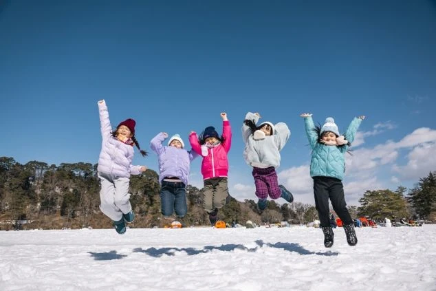冬の雪原で楽しそうにジャンプする5人の子供たち。スキー場や雪国でのリゾートバイトで、子供たちと触れ合う仕事や冬のレジャーを楽しみたい方に魅力的な画像。