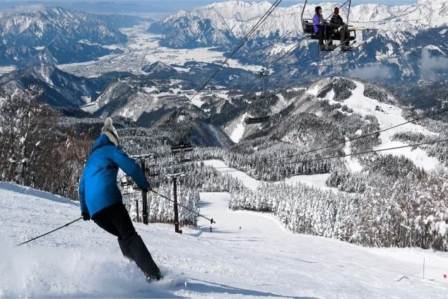 広大な雪山を背景に、スキーヤーが滑走する様子とスキーリフト。冬のリゾートバイトで、壮大な景色の中でスキー場スタッフやホテルスタッフとして働きたい方に訴求する画像。