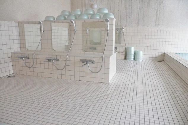 リゾートバイト寮の共用大浴場。シャワーブースが複数並び、湯桶も用意された、清潔感のある広い浴室の画像。