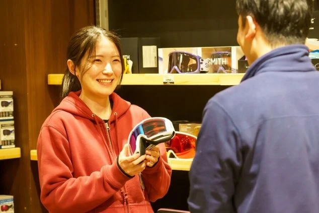 雪化粧した雄大な山々を背景に、ゲレンデに座って景色を眺めるスノーボーダーの後ろ姿。リゾートバイトでスキー場スタッフとして働きながら、絶景を楽しみたい方に魅力的な画像。