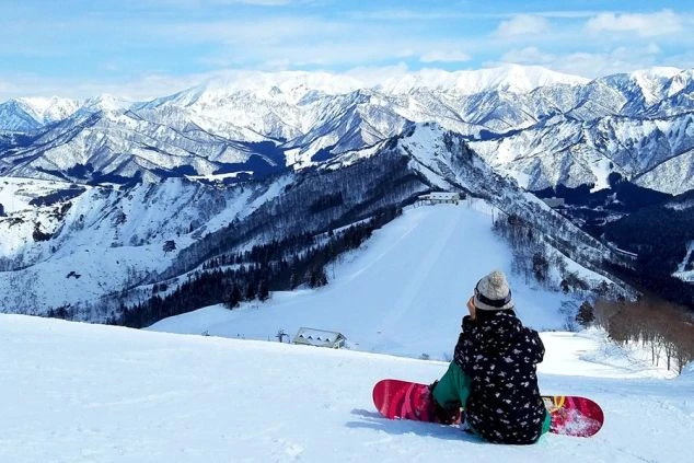 雪に覆われた広大な風景の中で、楽しそうにジャンプする厚着の人物。冬のリゾートバイトで、雪国での生活やウィンタースポーツを楽しみたい方に訴求する画像。