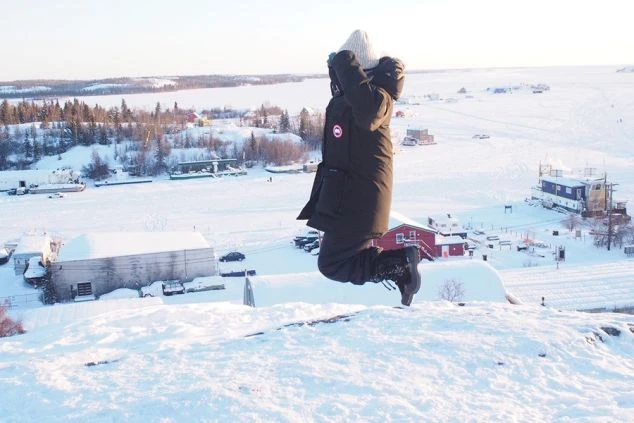 雪化粧した雄大な山々を背景に、ゲレンデに座って景色を眺めるスノーボーダーの後ろ姿。リゾートバイトでスキー場スタッフとして働きながら、絶景を楽しみたい方に魅力的な画像。