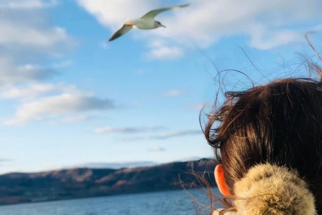 湖を見つめる女性の後ろ姿。空には鳥が飛んでおり、リゾート地での穏やかなひとときを感じさせる。