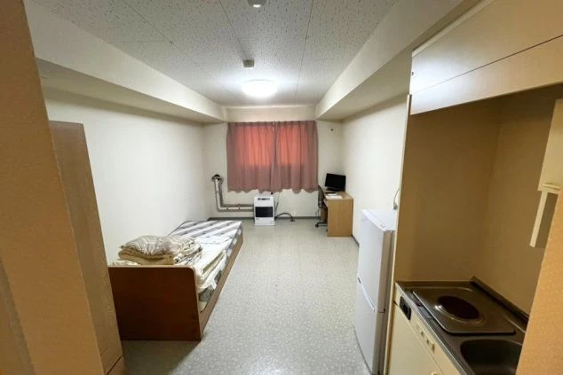 リゾートバイトの個室寮の部屋の画像。右にはキッチン・冷蔵庫、奥にはTV、暖房、ベッドが見える。