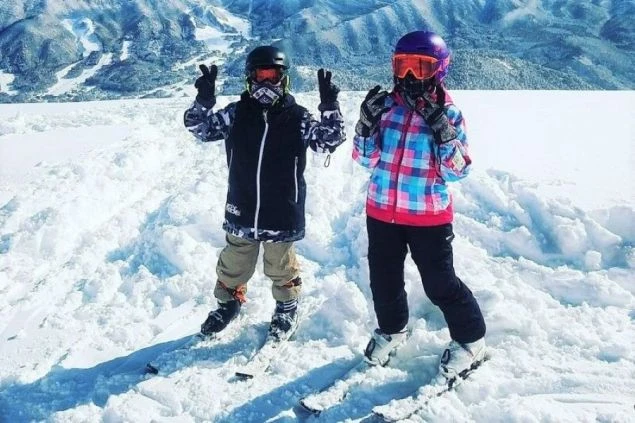 スキーウェアとヘルメットを着用し、雪山でポーズをとる2人のスキーヤー。冬のリゾートバイトの様子。