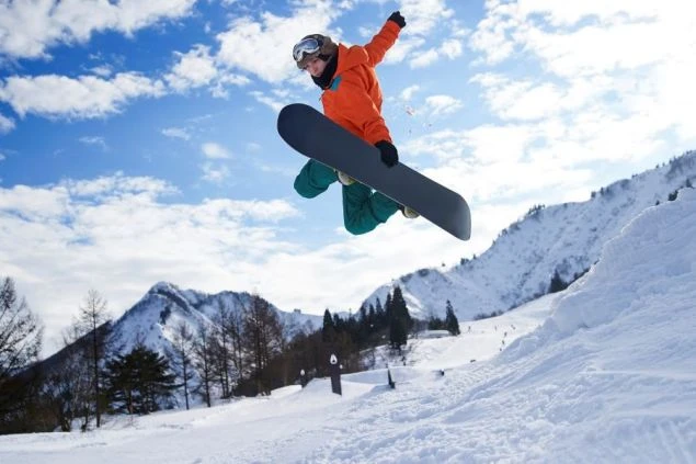青い空の下、スノーボードでジャンプする人物。雪山を背景に、ダイナミックなウィンタースポーツの瞬間。