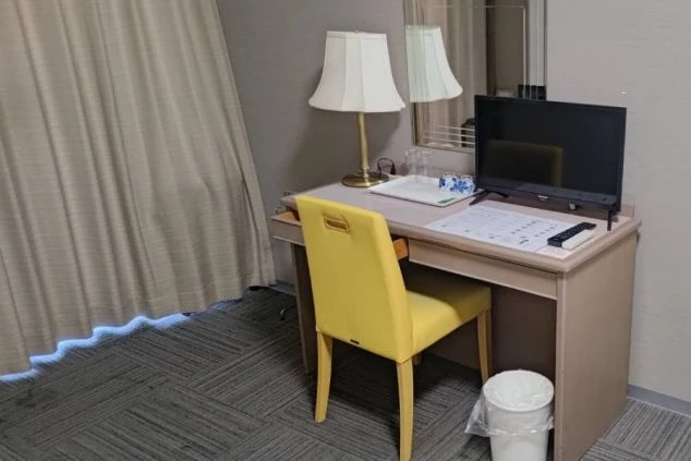 リゾートバイトの寮の部屋のデスクを撮影した画像。デスクの上にはテレビとスタンドライトが置かれ、黄色の椅子が目を引く。リゾートバイトの寮の部屋の画像。