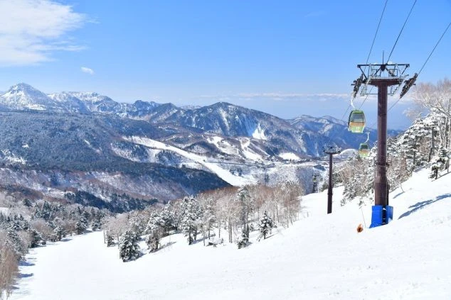  スキー場でスキーを楽しむ人々の画像。青い空と白い雲の下、雪山とリフトが広がり、リゾートバイトでウィンタースポーツを満喫している様子。