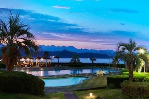 夜景が美しい、海の近くのリゾートホテルの屋外プールの画像。ヤシの木と山並みが見える南国リゾートバイトの求人。