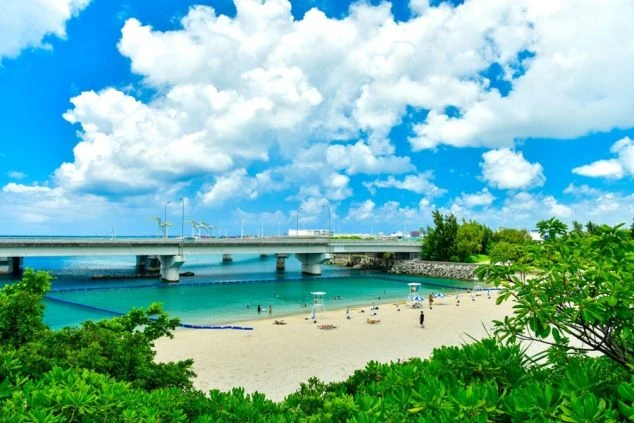 那覇市唯一の海水浴場、波の上ビーチ。透明度の高いエメラルドグリーンの海と白い砂浜の向こうに、大きな橋が見える都会のオアシス。