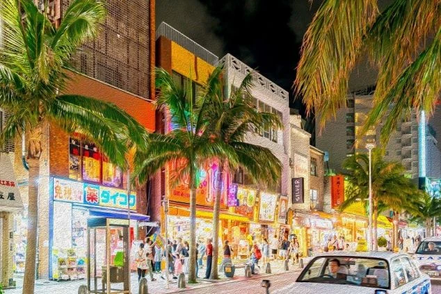 ネオンが輝く、夜の沖縄・国際通り。ヤシの木がライトアップされ、昼間とは違う華やかな雰囲気の中、多くの人々で賑わっている。