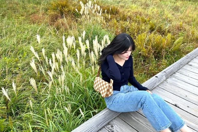 ススキが揺れる木道の端に座る女性のイメージ画像。リゾートバイトの休日を満喫。