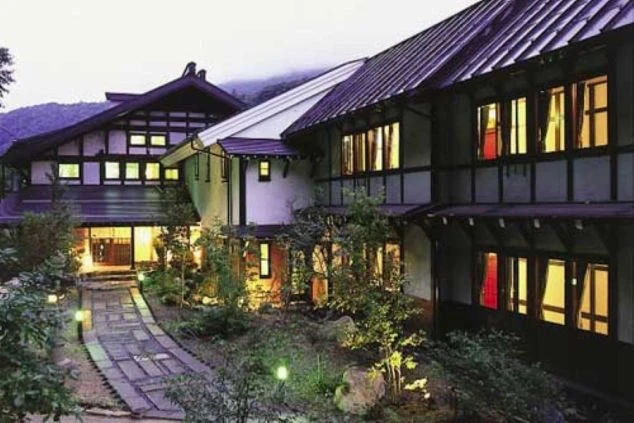 夜間にライトアップされた伝統的な旅館の建物外観。温かい光が漏れる窓と石畳の通路が映る職場のイメージ画像。