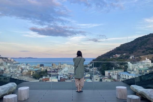 ワクトリでリゾートバイトをしたスタッフが撮影した、海と街並みが見渡せる展望台に立つ人物の後ろ姿が映るイメージ画像。リゾートバイトの休日を満喫。