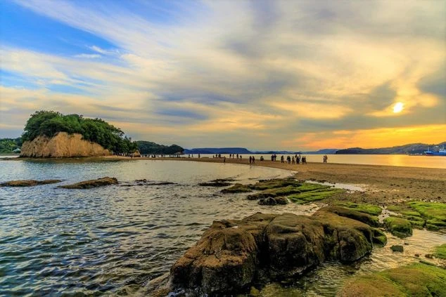 香川県小豆島のエンジェルロードの画像。干潮時に現れる砂の道が沖の島まで続き、多くの観光客が歩いている。夕暮れの空が美しく、リゾートバイトの休日に訪れたいロマンチックな景勝地。