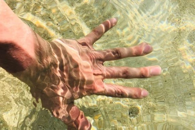  透明度の高い海に手を入れる様子を撮影した画像。リゾートバイトで訪れる沖縄や離島の美しい海を象徴し、休日のリフレッシュやマリンアクティビティを楽しめることを伝える画像。