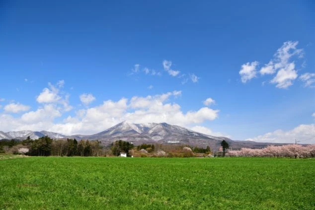 霧に包まれた山肌で、岩に腰掛けて休憩する女性。リゾートバイトの休日の過ごし方のイメージ。