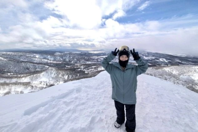 ワクトリでリゾートバイトをしたスタッフが撮影した、雪山の山頂でピースサインをする人物。壮大な雪景色と山々が広がる絶景のイメージ画像。リゾートバイトの休日を満喫。