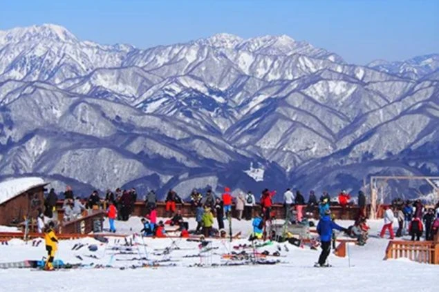 雪山の絶景を背景に、多くのスキー客が休憩しているゲレンデ。