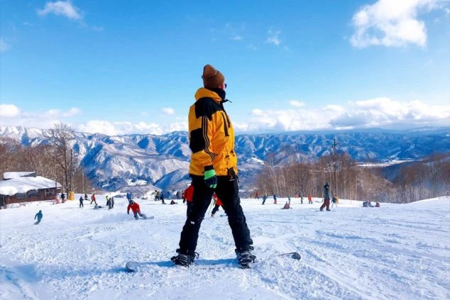 雪山を背景に、スノーボードを持つ男性がゲレンデでポーズをとる。