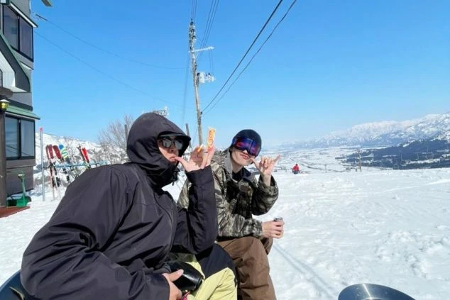 スキー場で休憩する若い二人。遠くに広がる雪山と青空の絶景。