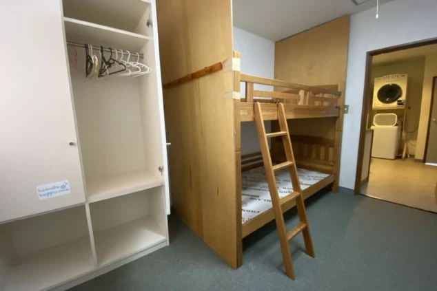 リゾートバイト相部屋寮の部屋の画像。部屋内に2段ベッドと収納が見え、入口から出て奥には洗濯機と乾燥機が見える。