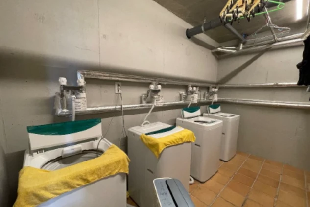 寮のランドリー。複数の洗濯機が並んだ清潔な共用スペースが映る。