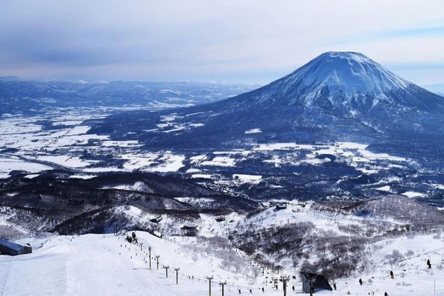 羊蹄山を背景にした広大なスキー場。多くのスキーヤーやスノーボーダーが滑走するイメージ画像。リゾートバイトの休日を満喫。