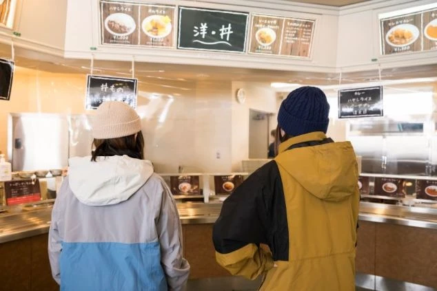 ゲレンデにあるレストランで、食事を選んでいる2人の画像。リゾートバイトの仕事中や休憩時間に食事をとる様子。