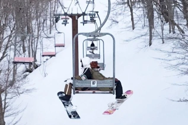 雪山のゲレンデで、スキーリフトに乗った2人が雪山を楽しんでいる画像。リゾートバイトの休日にスノーボードを満喫するイメージ。
