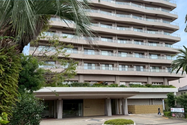 青空の下、大きなヤシの木に挟まれるように建つ、現代的な多層階の大型ホテルの外観。