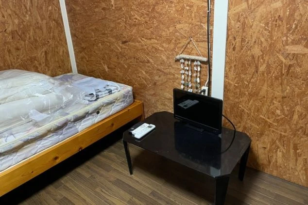 寮の居室。木製の壁と床、ベッド、テレビが備え付けられたシンプルな部屋。